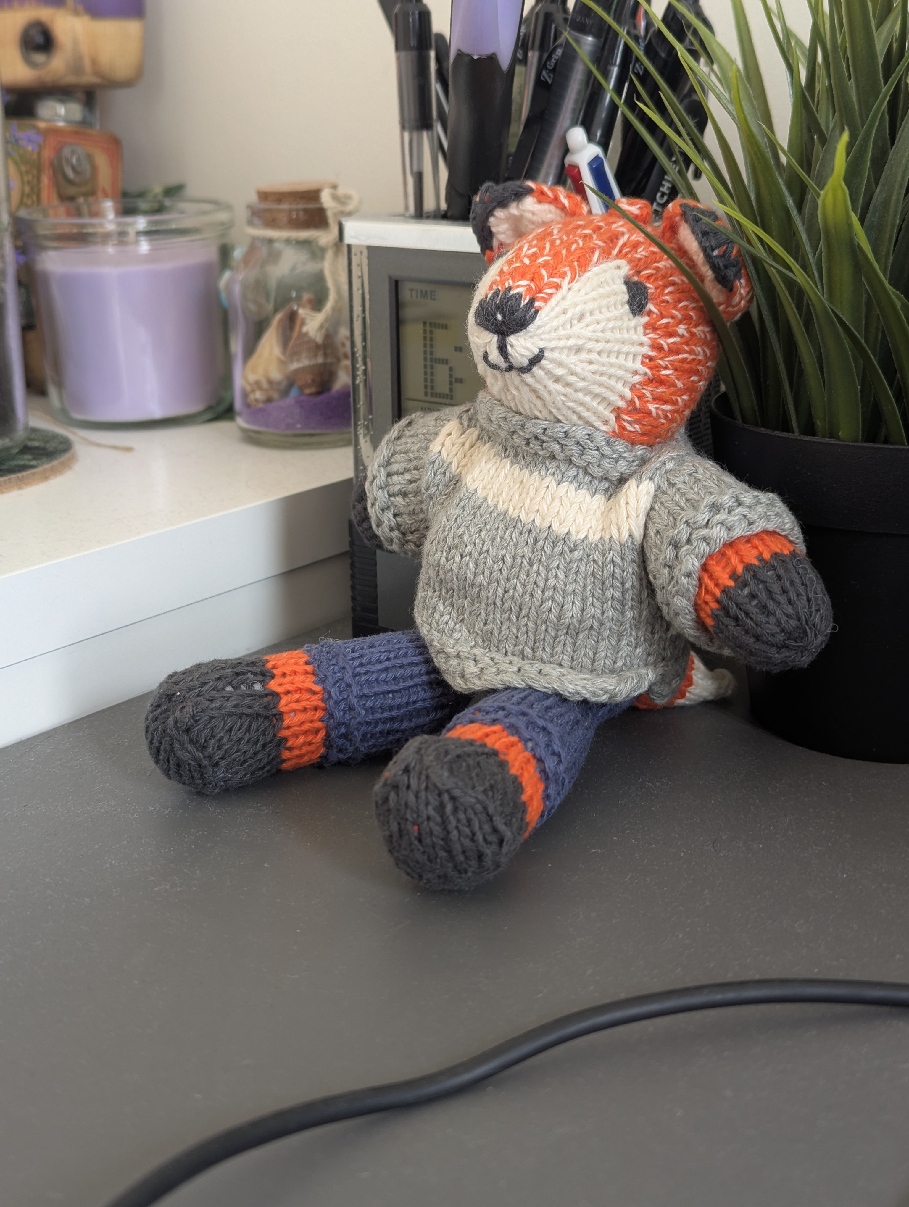 a soft fox plushie sitting on my desk. she is wearing a jumper and trousers